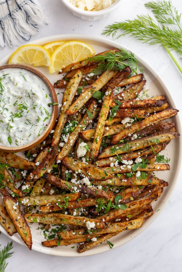 Greek fries on a large plate served with a bowl of dipping sauce