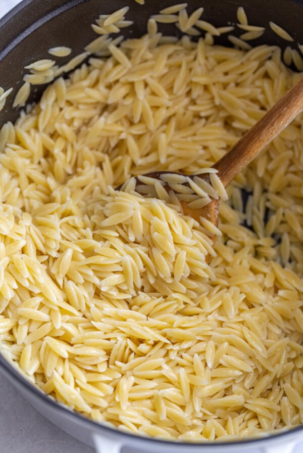 stirring cooked orzo with a wooden spoon