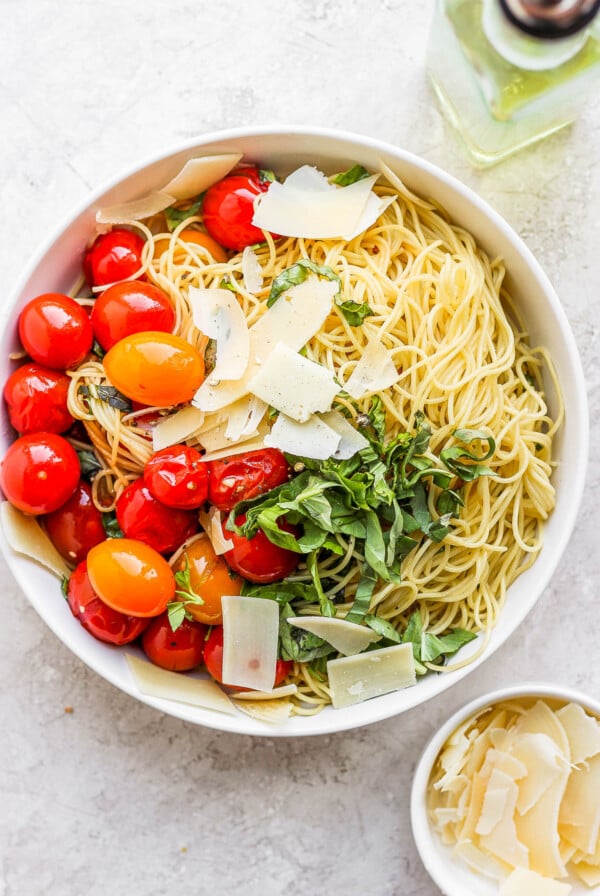 White bowl filled with pasta, tomatoes, basil and parmesan cheese.