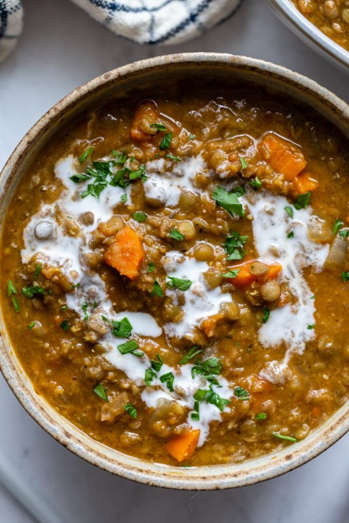 top down shot of a bowl of lentil soup with carrots in it. it's topped with a cream sauce and chopped parsley